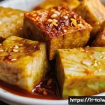 중화민국 대표 간식 - A close-up, eye-level shot of a serving of Taiwanese Stinky Tofu (Chòu dòufu) at a bustling night ma...